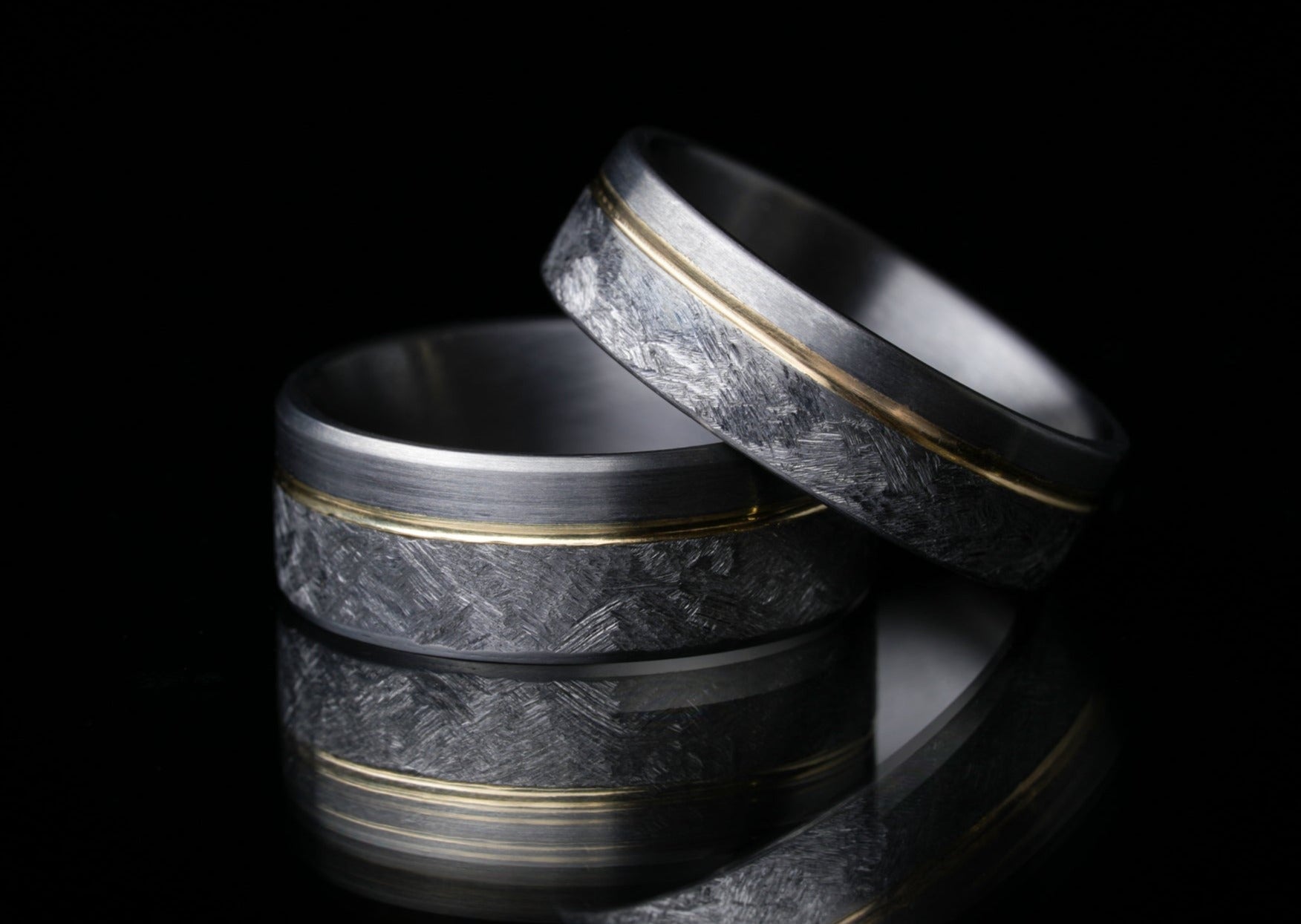 Stacked 8mm 'Rae' tantalum rings with 14k gold inlay on reflective surface