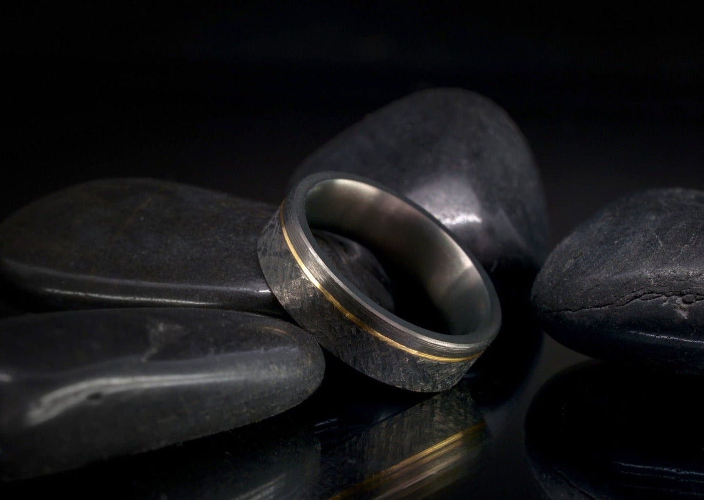 Black zirconium ring with 14k gold inlay resting on dark stones